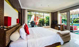 Hotellihuone, jossa on suuri sänky valkoisilla vuodevaatteilla ja punaisilla tyynyillä, ja se sijaitsee suuren ikkunan edessä, josta on näkymä puutarhaan. (Tekoälyn luoma teksti)