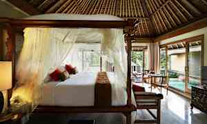 Makuuhuone, jossa on pylvässänky, valkoiset verhot ja punaiset tyynyt. Lattiasta kattoon ulottuvat ikkunat päästävät päivänvalon huoneeseen, ja näkymä sisältää pienen uima-altaan ja vihreää kasvillisuutta. (Tekoälyn luoma teksti)