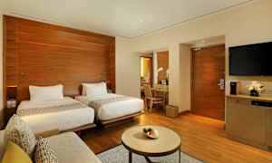 Moderni hotellihuone, jossa on kaksi erillistä vuodetta, kirjoituspöytä peilin kanssa, sohva ja pieni pöytä. (Tekoälyn luoma teksti)