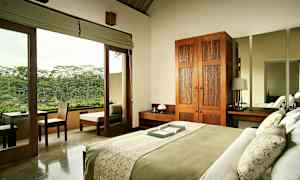 Makuuhuone, jossa on vihreällä ja valkoisella vuodevaatteella pedattu sänky. Huoneessa on puinen vaatekaappi, yöpöytä ja iso peili. Lasiovet johtavat parvekkeelle, jolta avautuu näkymä vehreään luontoon. (Tekoälyn luoma teksti)