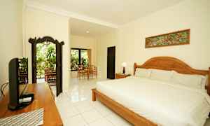 Tyylikkäästi sisustettu ja valoisa makuuhuone, jossa suuri sänky, puukoristeita ja istuinalue ikkunan ääressä, josta on näkymä vehreyteen. (Tekoälyn luoma teksti)