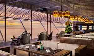 Ravintola, jossa istumapaikkoja rottinkihuonekaluilla ja näkymä merelle auringonlaskun aikaan. (Tekoälyn luoma teksti)