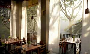 Valoisa ja ilmava ravintola-alue, jossa on korkeat ikkunat, jotka päästävät sisään luonnonvaloa, ja näkymä ympäröiviin puihin. (Tekoälyn luoma teksti)