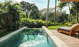 Kuva uima-altaasta, jossa kirkasta vettä, ympärillä vehreää kasvillisuutta ja aurinkotuoli puisella terassilla. (Tekoälyn luoma teksti)