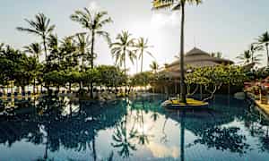 Uima-allas, jota ympäröivät palmut ja kasvillisuus, taustalla olkikattoinen maja. (Tekoälyn luoma teksti)