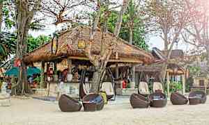 Olkihuopakattoinen rantabaari, jota ympäröivät puut ja punotut rottinkikalusteet. (Tekoälyn luoma teksti)