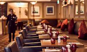 Kuvassa näkyy ravintola, jossa on katettuja pöytiä, punaisia laseja ja tummia tuoleja. (Tekoälyn luoma teksti)