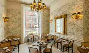 Ravintolan sisätila klassisella sisustuksella, pöytiä ja tuoleja, iso peili ja kattokruunu. (Tekoälyn luoma teksti)