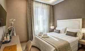 Hotellihuone, jossa on parivuode, valkoiset ja beige lakanat, kirjoituspöytä, lamppu ja seinälle kiinnitettävä TV. (Tekoälyn luoma teksti)