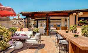 Ulkoilmaterassi, jossa on istuimia, pöytiä ja vihreitä kasveja kirkkaan sinisen taivaan alla. (Tekoälyn luoma teksti)