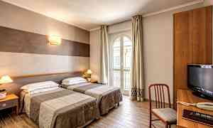 Hotellihuone, jossa kaksi erillistä vuodetta, työpöytänurkkaus ja suuri ikkuna, josta tulee päivänvaloa sisään. (Tekoälyn luoma teksti)