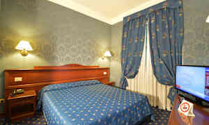 Hotellihuone sinisellä sisustuksella, mukaan lukien sänky, verhot ja tapetti, sekä televisio sivussa. (Tekoälyn luoma teksti)