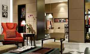 Tyylikkäästi sisustettu olohuone, jossa on punaisia ja beigejä tuoleja, kukkia ja kirjahyllyjä. (Tekoälyn luoma teksti)