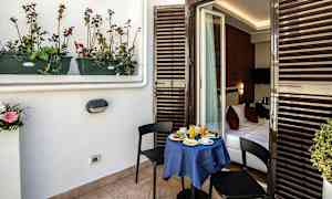 Parveke, jossa pieni pöytä katettu aamiaiselle ja kaksi tuolia. Pöydällä on sininen liina, ja parveke johtaa makuuhuoneeseen. (Tekoälyn luoma teksti)