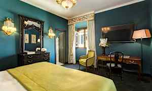 Tyylikkäästi sisustettu hotellihuone, jossa vihreä peite, kirjoituspöytä, peili ja verhot avoimen ikkunan edessä. (Tekoälyn luoma teksti)