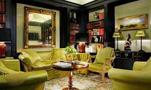 Tyylikkäästi sisustettu olohuone, jossa on vihreällä verhoillut huonekalut, sohvapöytä ja kirjavarastoja täynnä kirjoja. (Tekoälyn luoma teksti)