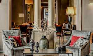 Kaksi nojatuolia tyynyillä pöydän edessä, jossa koriste-esineitä, elegantissa sisustetussa ympäristössä. (Tekoälyn luoma teksti)