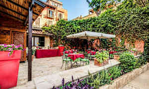 Ulkotila, jossa pöytiä ja tuoleja sekä vihreää kasvillisuutta. (Tekoälyn luoma teksti)