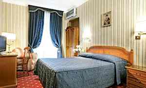 Hotellihuone, jossa parisänky sinisellä päiväpeitteellä, kirjoituspöytä, nojatuoli ja siniset verhot. (Tekoälyn luoma teksti)