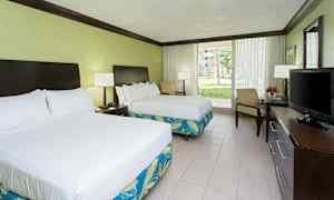 Hotellihuone, jossa on kaksi parivuodetta, työpöytä televisiolla ja suuret lasiovet, jotka avautuvat puutarhaan. (Tekoälyn luoma teksti)