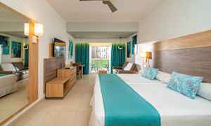 Hotellihuone, jossa on parivuode ja sinisiä yksityiskohtia. Huoneessa on myös sohva, työpöytä ja parveke näkymällä. (Tekoälyn luoma teksti)