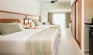 Hotellihuone, jossa kaksi sänkyä, vaalea sisustus ja suuret ikkunat. (Tekoälyn luoma teksti)