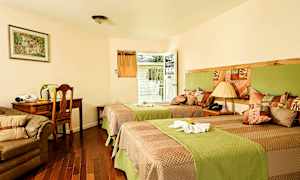 Hotellihuone, jossa on kaksi yhden hengen vuodetta, sohva, kirjoituspöytä ja tuoli. Huoneesta on myös ovi parvekkeelle. (Tekoälyn luoma teksti)