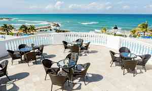 Terassi, jossa pöytiä ja tuoleja, merinäköala ja palmupuita. (Tekoälyn luoma teksti)