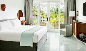 Valoisa ja tyylikäs hotellihuone, jossa on suuri sänky, nojatuoli ja kalusteita puuyksityiskohdilla. Huoneessa on suuret lasiovet, jotka johtavat parvekkeelle vehreiden palmujen näkymiin. (Tekoälyn luoma teksti)