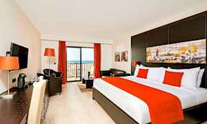 Hotellihuone, jossa sänky, istuinryhmä ja parvekkeen ovi. (Tekoälyn luoma teksti)