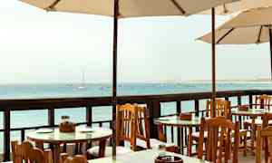 Ulkoilmapöytiä ja tuoleja varjojen alla merinäkymällä. (Tekoälyn luoma teksti)