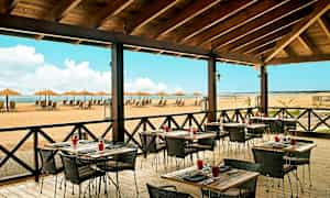 Ravintola ulkoterassilla ja näkymä rannalle, jossa on aurinkotuoleja ja varjoja. (Tekoälyn luoma teksti)