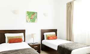 Huone, jossa kaksi erillistä vuodetta, yöpöytä ja seinäkoriste. (Tekoälyn luoma teksti)