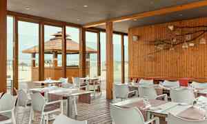 Ravintola, jossa puupaneelit ja lasiseinät, näkymä rannalle. (Tekoälyn luoma teksti)