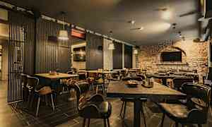 Ravintola, jossa on puupöytiä ja tuoleja sekä tiiliseinät. (Tekoälyn luoma teksti)