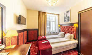 Hotellihuone, jossa kaksi yhden hengen sänkyä, punaiset päiväpeitot ja valaisimet. (Tekoälyn luoma teksti)