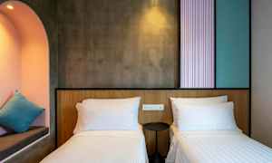 Hotellihuone, jossa on kaksi yhden hengen vuodetta, pieni pyöreä yöpöytä ja sisäänrakennettu syvennys, jossa tyyny. (Tekoälyn luoma teksti)