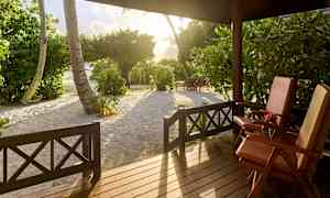 Näkymä verannalta, jossa on kaksi aurinkotuolia, puita ja hiekkaa auringonlaskun valossa. (Tekoälyn luoma teksti)