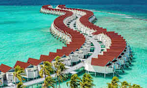 Tyylikkäitä veden päällä olevia bungaloweja, joiden punaiset katot ovat värikkään sinisen veden päällä. (Tekoälyn luoma teksti)