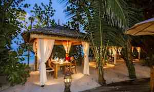 Valaistu terassi katolla ja valkoisilla verhoilla, ympärillä vehreyttä rannalla. (Tekoälyn luoma teksti)