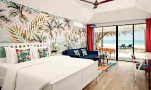 Hotellihuone, jossa on parivuode, sohva ja suuri lasiovi, joka avautuu rannalle, jossa on palmuja ja merinäköala. (Tekoälyn luoma teksti)