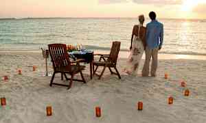 Pariskunta seisoo rannalla meren äärellä, edessään pöytä tuoleineen ja kynttilöineen. (Tekoälyn luoma teksti)