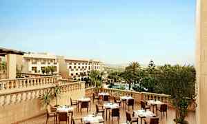 Hotellin ulkoterassi katettujen pöytien kanssa, ympäröity palmupuiden ja näkymä maisemaan. (Tekoälyn luoma teksti)