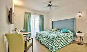 Hotellihuone, jossa on parivuode, koristeelliset tyynyt ja pöytä kahdella tuolilla. (Tekoälyn luoma teksti)