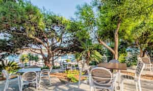 Ulkoterassi varjoavien puiden alla, jossa on pöytiä ja tuoleja. (Tekoälyn luoma teksti)