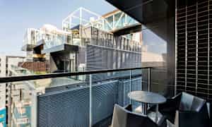 Parveke, jossa on moderni sisustus, mukaan lukien pyöreä pöytä ja tuolit, näkymät rakennukseen, jossa on lasi- ja metallijulkisivuja. (Tekoälyn luoma teksti)