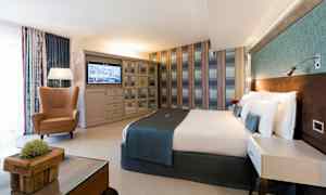 Hotellihuone, jossa on parivuode, nojatuoli, pöytä ja televisio seinällä. (Tekoälyn luoma teksti)