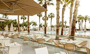 Ulkona sijaitseva ravintola, jossa on useita pöytiä ja tuoleja, ympäröitynä palmuilla ja näkymällä uima-altaalle. (Tekoälyn luoma teksti)