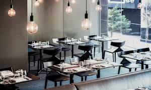 Moderni ravintola, jossa tyylikkäästi katetut pöydät ja roikkuvat lamput. (Tekoälyn luoma teksti)