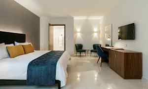 Hotellihuone, jossa on parivuode, kirjoituspöytä, kaksi nojatuolia ja seinään kiinnitetty televisio. (Tekoälyn luoma teksti)